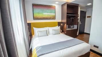 A hotel room with a large bed, a headboard, a painting, a wardrobe, and a kitchenette.