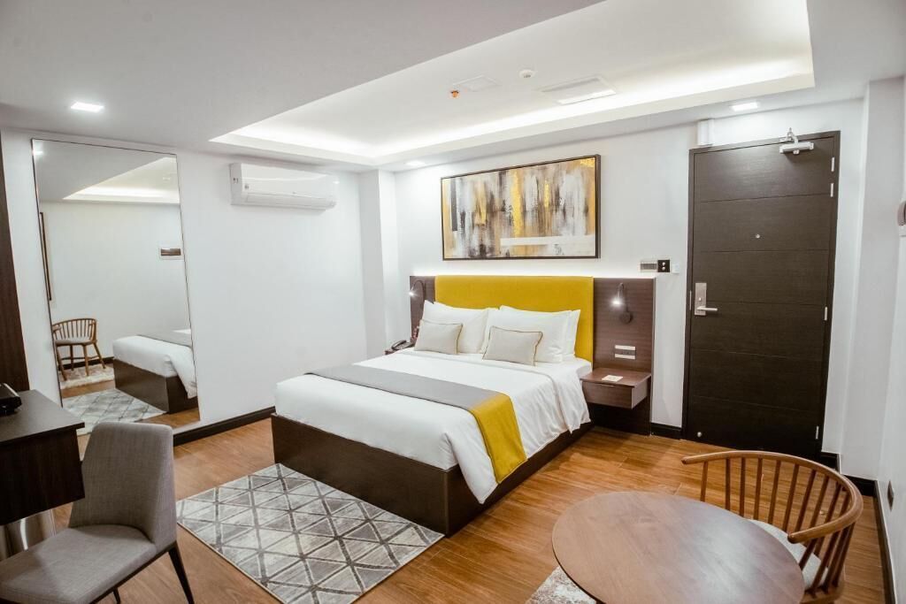 Una habitación de hotel moderna con cama, mesitas de noche, escritorio, silla y mesa de comedor.
