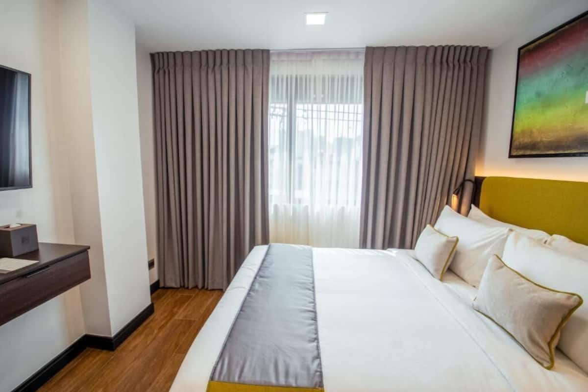 Ein Hotelzimmer mit Bett, Vorhängen, Schreibtisch und einem Bild an der Wand.