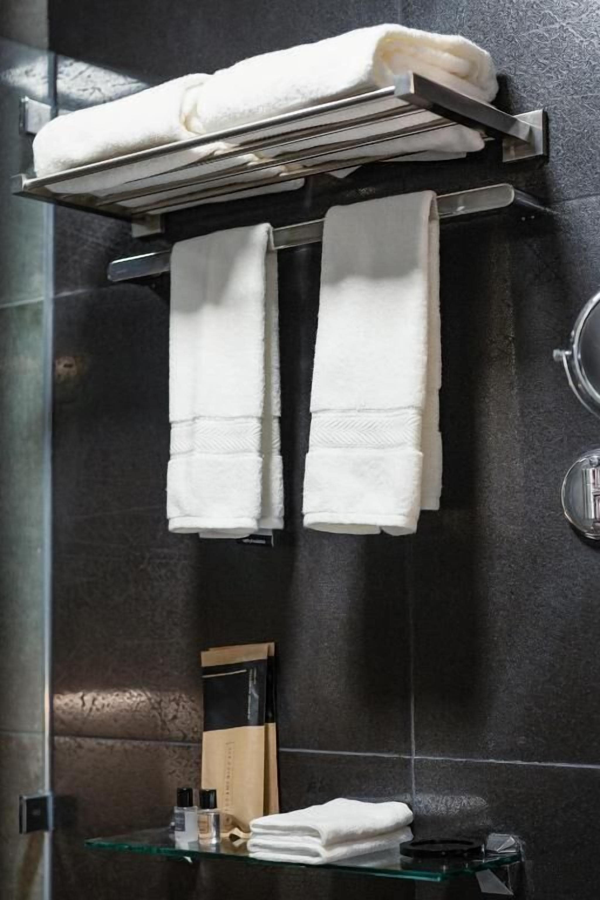 A bathroom with a glass shower enclosure, a towel rack with two towels, and a glass shelf with toiletries.