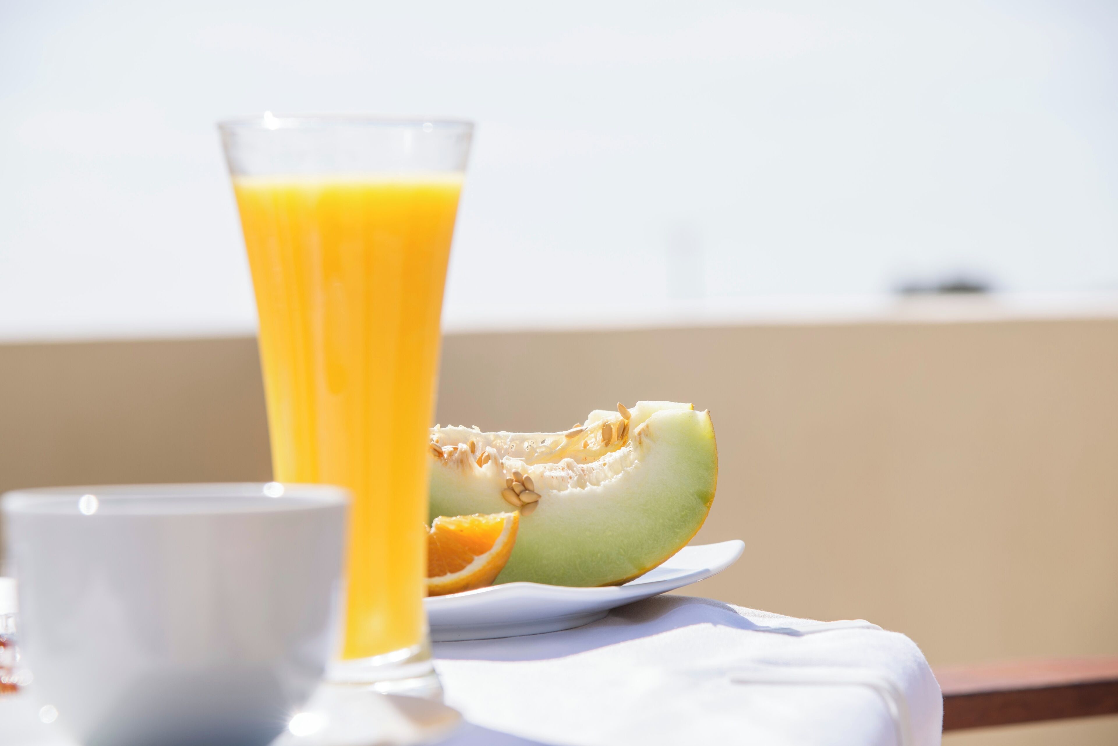 Un vaso de zumo de naranja y media sandía en un plato blanco, con una taza blanca al frente.