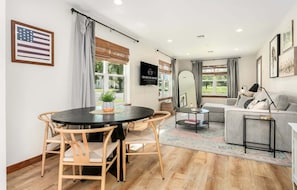 Ein modernes Wohnzimmer mit rundem Tisch, zwei Stühlen, einer Couch, einem Fernseher und einem Fenster mit Jalousien.