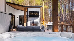 A modern outdoor living area with a hot tub, a fireplace, and a screened-in seating area. - NEW! 4 King Suites, Hot Tub, Fire Pit, Outdoor Lounge, Spacious (Broken Bow)