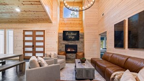 A cozy log cabin interior with a fireplace, leather sofas, and a dining area. - NEW! 4 King Suites, Hot Tub, Fire Pit, Outdoor Lounge, Spacious (Broken Bow)