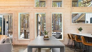 A modern interior with a long dining table, wooden walls, and large windows. - NEW! 4 King Suites, Hot Tub, Fire Pit, Outdoor Lounge, Spacious (Broken Bow)