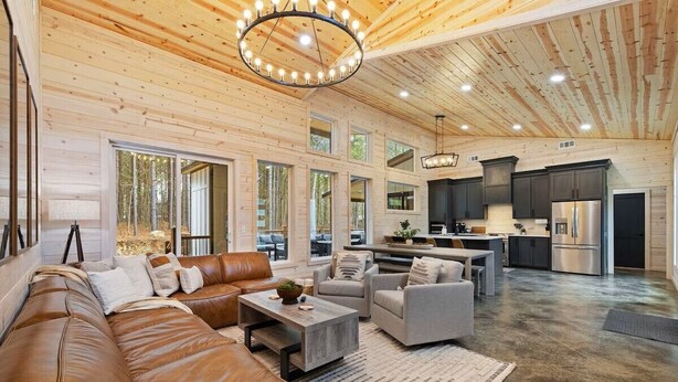 A spacious living area with a brown leather sofa, a coffee table, and a kitchen with stainless steel appliances. - NEW! 4 King Suites, Hot Tub, Fire Pit, Outdoor Lounge, Spacious (Broken Bow)
