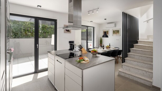 A modern kitchen with a central island, a dining area, and a staircase leading to an upper level. - House Explorer One (Istria - Funtana) (Funtana)