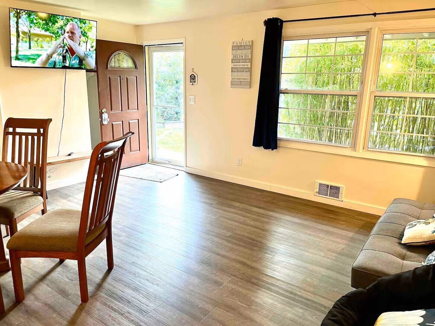 Una sala de estar con televisor, un comedor con sillas, un ventanal con cortinas y una puerta que da al exterior.