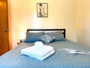 A neatly made bed with a blue quilt, two pillows, a folded white towel, and a patterned pillow on a wooden headboard. - Beautiful 4-bedroom house in Lynnwood perfect for your getaway (Lynnwood)