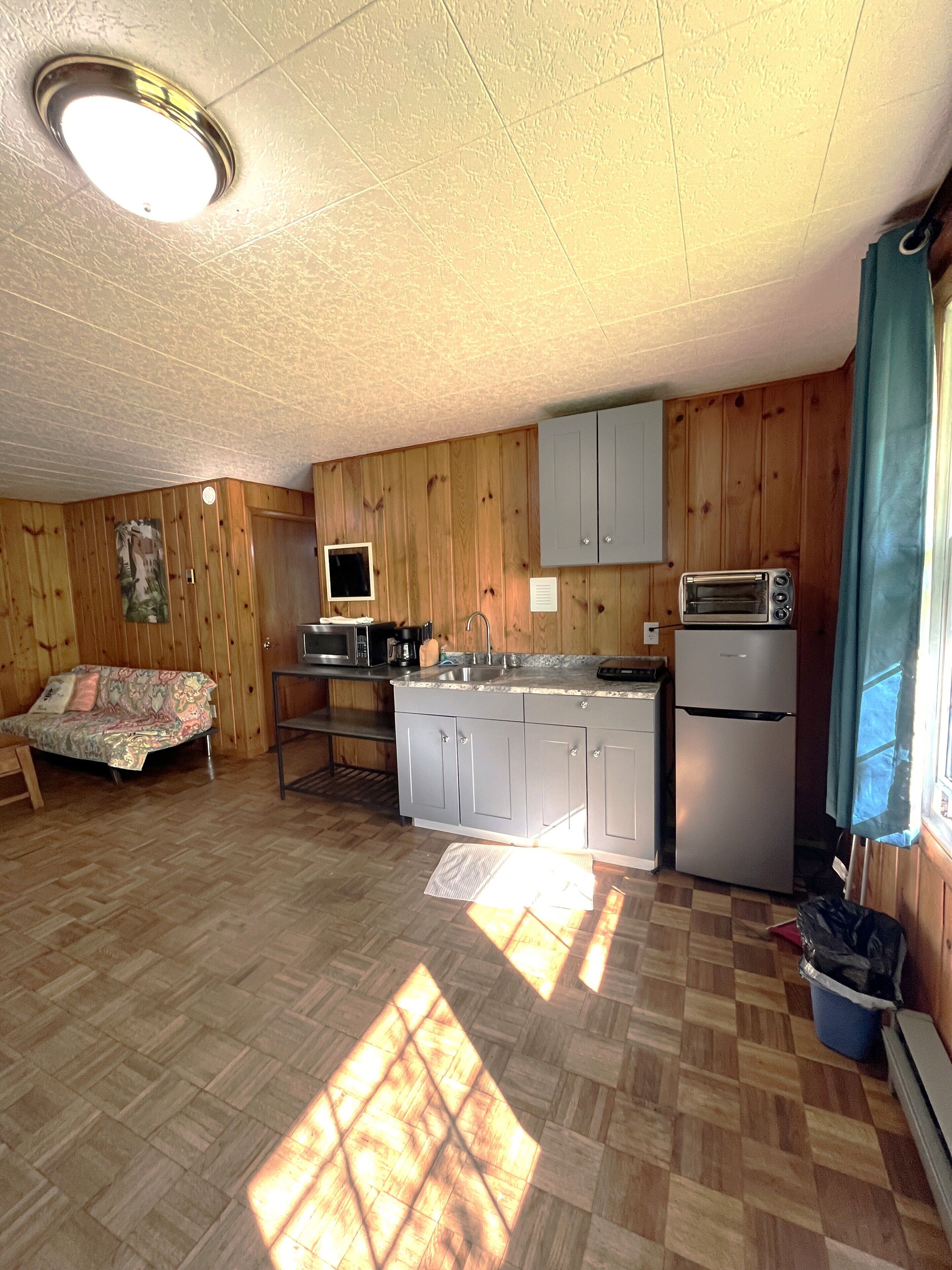 A compact kitchen with wooden paneling, a built-in microwave, a toaster oven, and a sink.