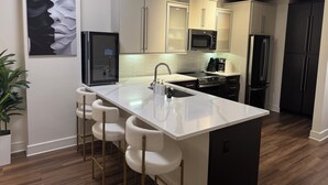 A modern kitchen with a central island, bar stools, stainless steel appliances, and a hexagonal backsplash.