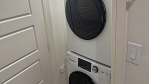 A laundry room with a front-loading washer and dryer, a door, and a light switch on the wall.