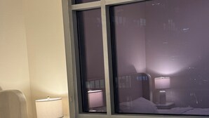 A hotel room with a bed, a nightstand with a lamp, and a window with a view of the city at night.