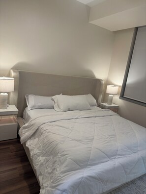 A neatly made bed with white bedding, two bedside tables with lamps, and a plain wall. - Skyview Downtown All Glass 1 Bedroom Cozy Apartment (Dallas)