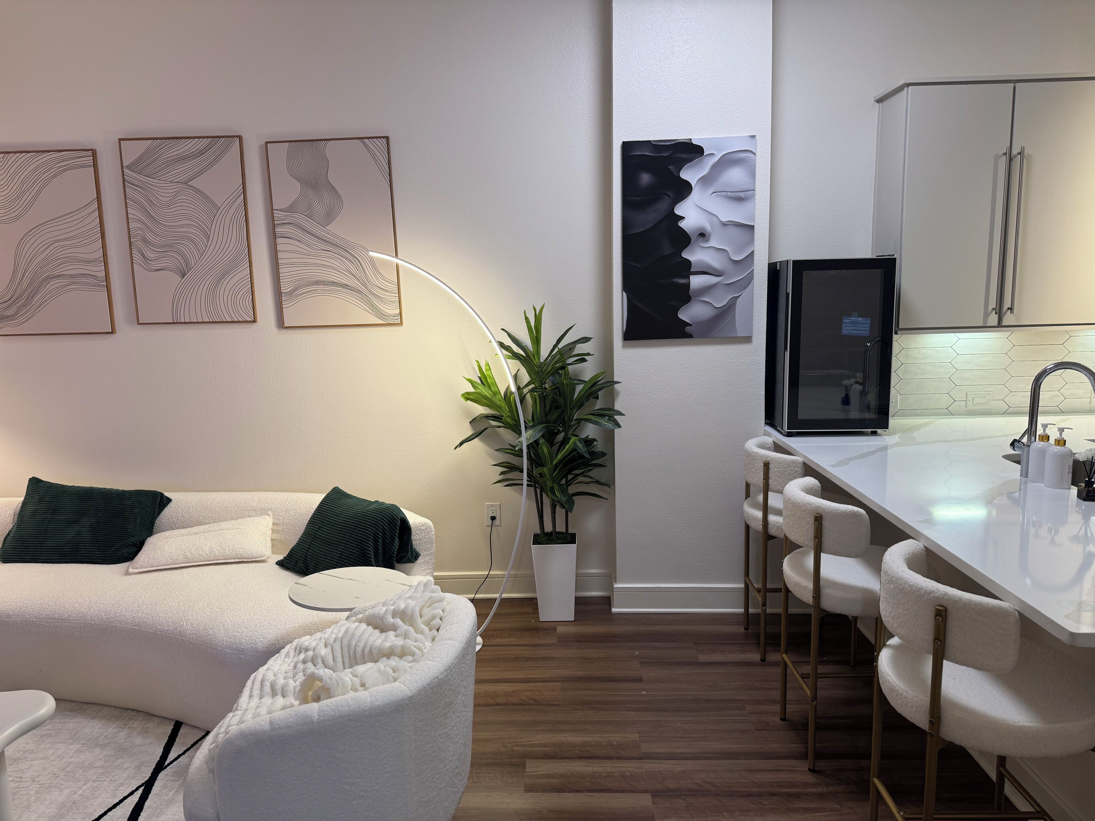 Un espace de vie moderne comprenant un canapé, un fauteuil blanc, une plante et un coin cuisine avec un bar.