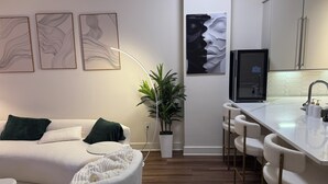 A modern living space with a sofa, a white armchair, a plant, and a kitchen area with a bar.