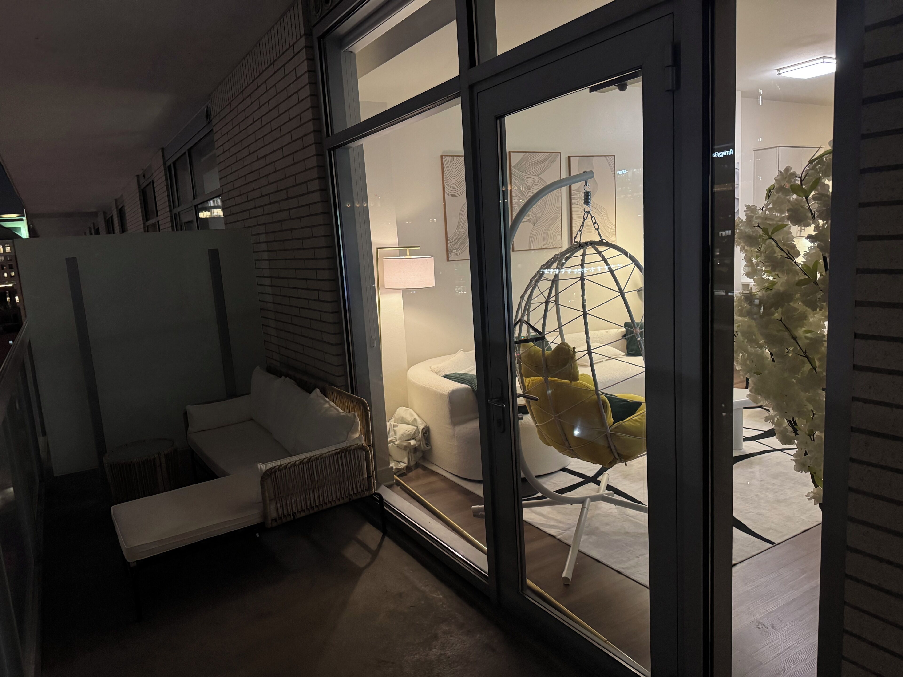 A modern hotel room with a glass door, a hanging chair, a white sofa, and a visible bathroom.