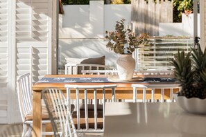 Un espace de restauration en plein air avec une table en bois, des chaises blanches et un vase décoratif rempli de fleurs.