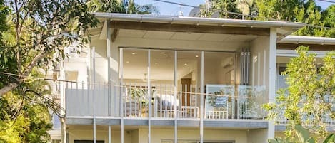A two-story residential building with a balcony on the upper floor, a white fence, and a number '28' on the gate.