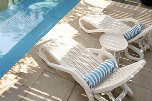 Duas poltronas brancas com almofadas listradas à beira da piscina.