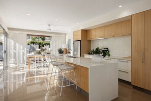 Eine moderne Küche mit einer zentralen Kochinsel, Barhocker, Holzschränken und einem Edelstahlkühlschrank.