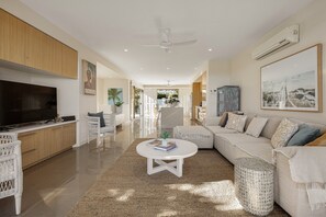 Ein modernes Wohnzimmer mit Fernseher, einem weißen Sofa, einem Couchtisch und einem Deckenventilator.