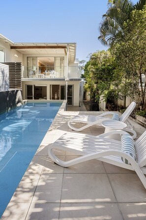 Ein modernes, zweistöckiges Haus mit Swimmingpool, Gartenmöbeln und einer überdachten Terrasse.