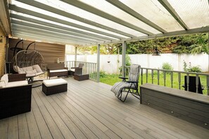 A covered deck with wicker furniture, a swing chair, and a view of a backyard. - Spacious 4BR Home with Garden and Parking (London)