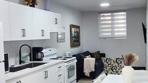 Una cocina moderna con armarios blancos, un comedor con mesa y sillas blancas, una estufa y un lavaplatos.