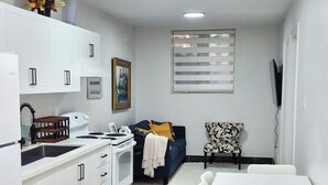Una cocina moderna con armarios blancos, una mesa de comedor con sillas, un sofá y un televisor montado en la pared.