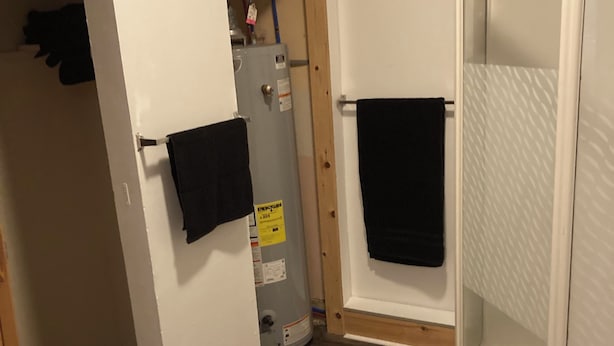 A bathroom with a shower, a towel rack, a heater, and a wooden floor.
