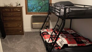 A bunk bed with a patterned bedspread, a dresser with decorative items, and a framed picture on the wall.
