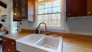 A kitchen with a double sink, wooden cabinets, a window with a view of trees, and a light fixture above the sink. - Lake Home with private dock (Gainesville)