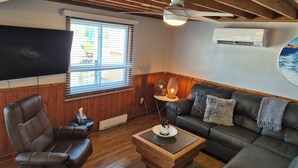 A room with a ceiling fan, a TV, a couch, a coffee table, and a window with blinds.