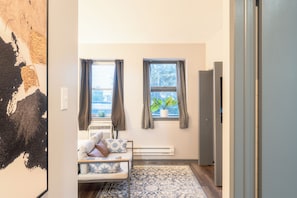 A room with a bed, a radiator, and two windows with curtains. - Charming 1-bedroom studio with AC in vibrant Chicago (Chicago)