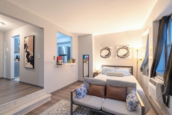 A modern bedroom with a bed, a sofa, a small kitchen area, and a staircase. - Charming 1-bedroom studio with AC in vibrant Chicago (Chicago)