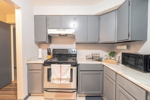 A compact kitchen with grey cabinets, a stainless steel oven, a microwave, and a sink. - Charming 1-bedroom studio with AC in vibrant Chicago (Chicago)