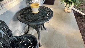 Une terrasse couverte avec une table et des chaises, un pot de fleurs et une vue sur la rue.