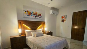 Une chambre à coucher comprenant un lit, des tables de chevet, une tête de lit, des œuvres d’art murales et un appareil de climatisation.