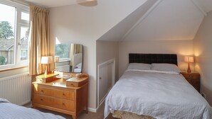Ein Schlafzimmer mit Bett, Kommode, Spiegel und Fenster mit Vorhängen.