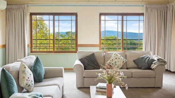 A room with two sofas, a coffee table, and large windows with a view of greenery and hills. - Twilight Ridge (Bega Valley)