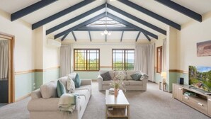 A spacious living room with a high ceiling, two sofas, a coffee table, and a painting on the wall. - Twilight Ridge (Bega Valley)