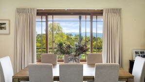 A dining area with a table, chairs, and a view of greenery through large windows. - Twilight Ridge (Bega Valley)
