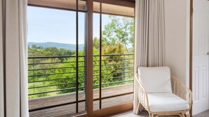 A balcony with a view of greenery and hills, a wicker chair, and a door. - Twilight Ridge (Bega Valley)
