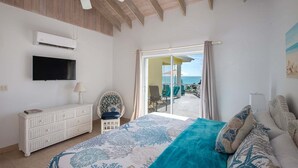 Et soveværelse med seng, fjernsyn, ventilator, et vindue med udsigt og en balkon med stole.