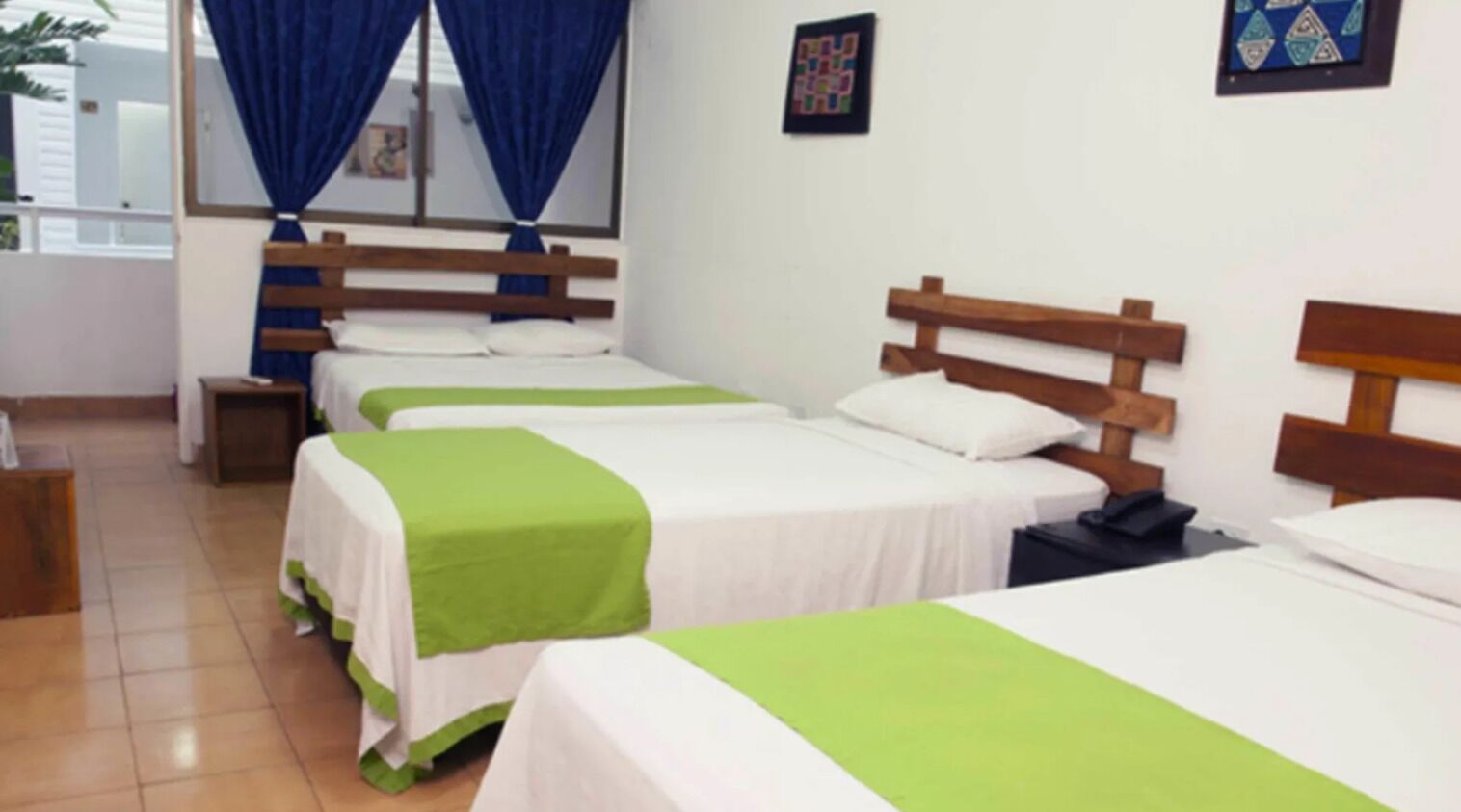 Una habitación de hotel con cuatro camas individuales, cada una con cabecero de madera y ropa de cama blanca.