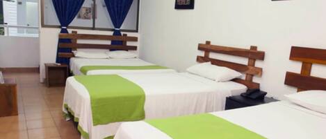 Una habitación de hotel con cuatro camas individuales, cada una con cabecero de madera y ropa de cama blanca.