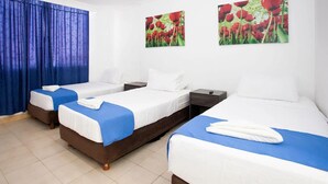 A hotel room with three beds, a blue curtain, and two wall-mounted flower paintings.