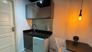 A compact kitchen with a black countertop, a small fridge, a sink, and a chair.