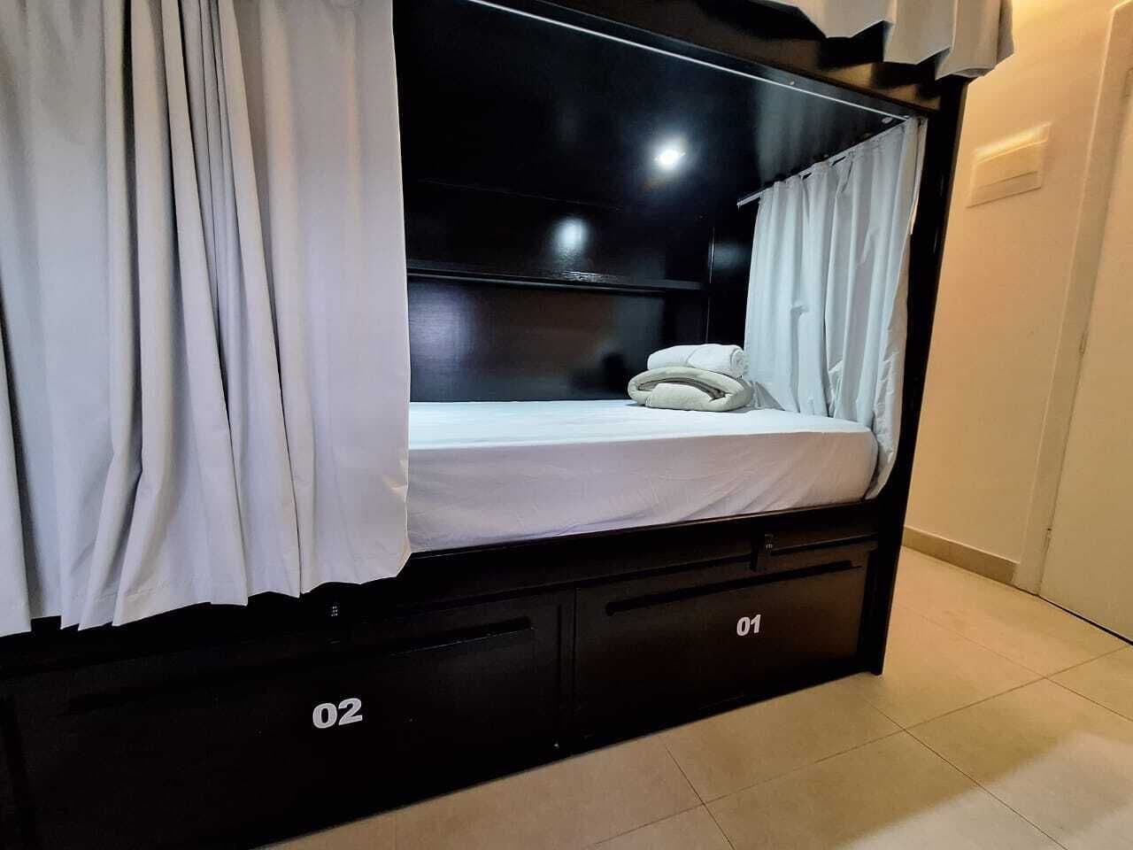 Uma cama beliche com colchão branco, cortinas brancas e cabeceira preta.
